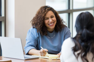 The mature adult female business owner smiles encouragingly at an unrecognizable female job applicant.