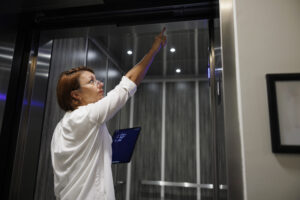 Elevator safety assessment: mature female claim agent using digital tablet to inspect and evaluate lift elevator in the condominium hall